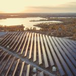 Estação de painéis solares com reflexo de sol e rio ao fundo. Sistema ECO